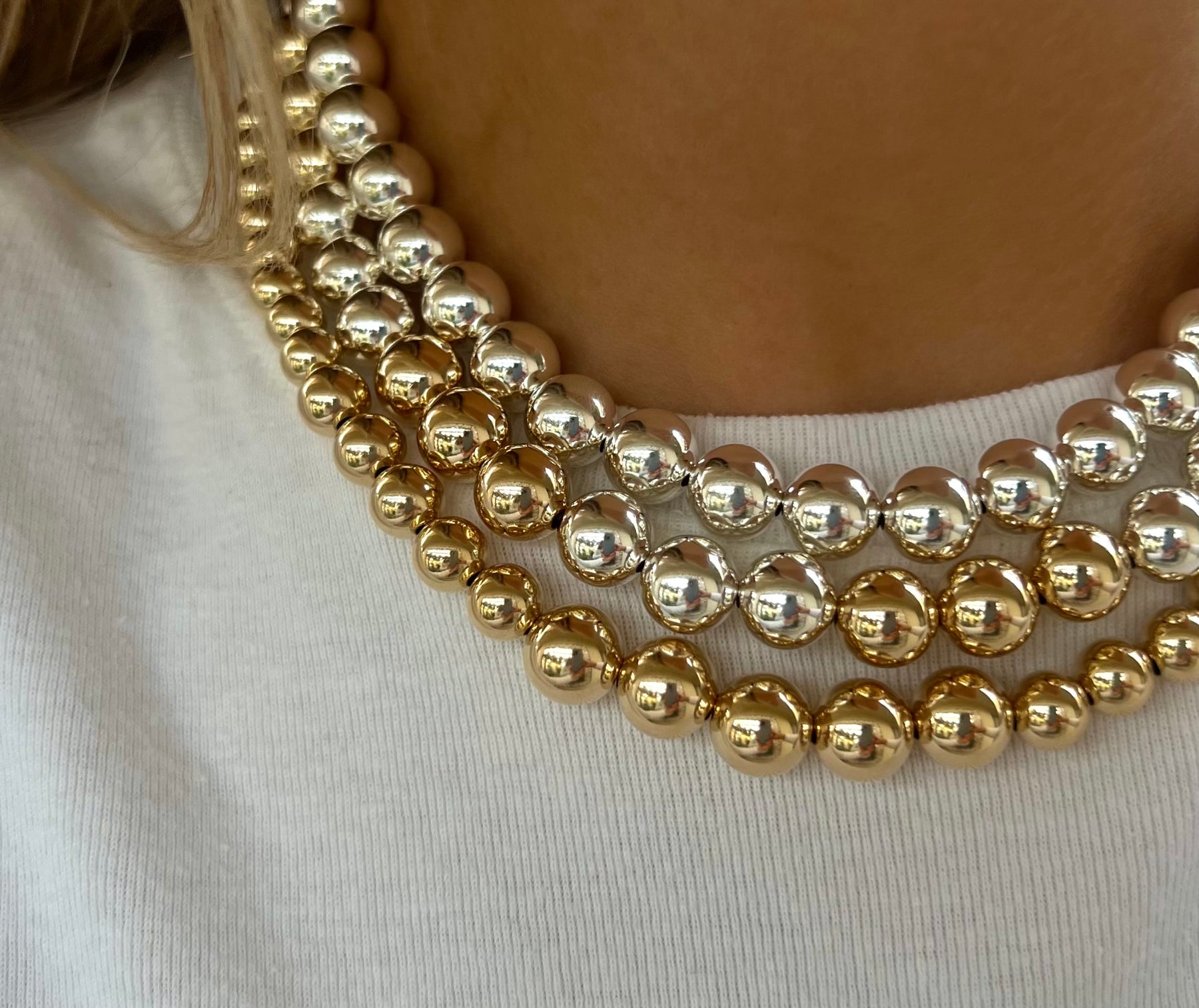 Close-up of a layered gold bead and crystal necklace on a white shirt.